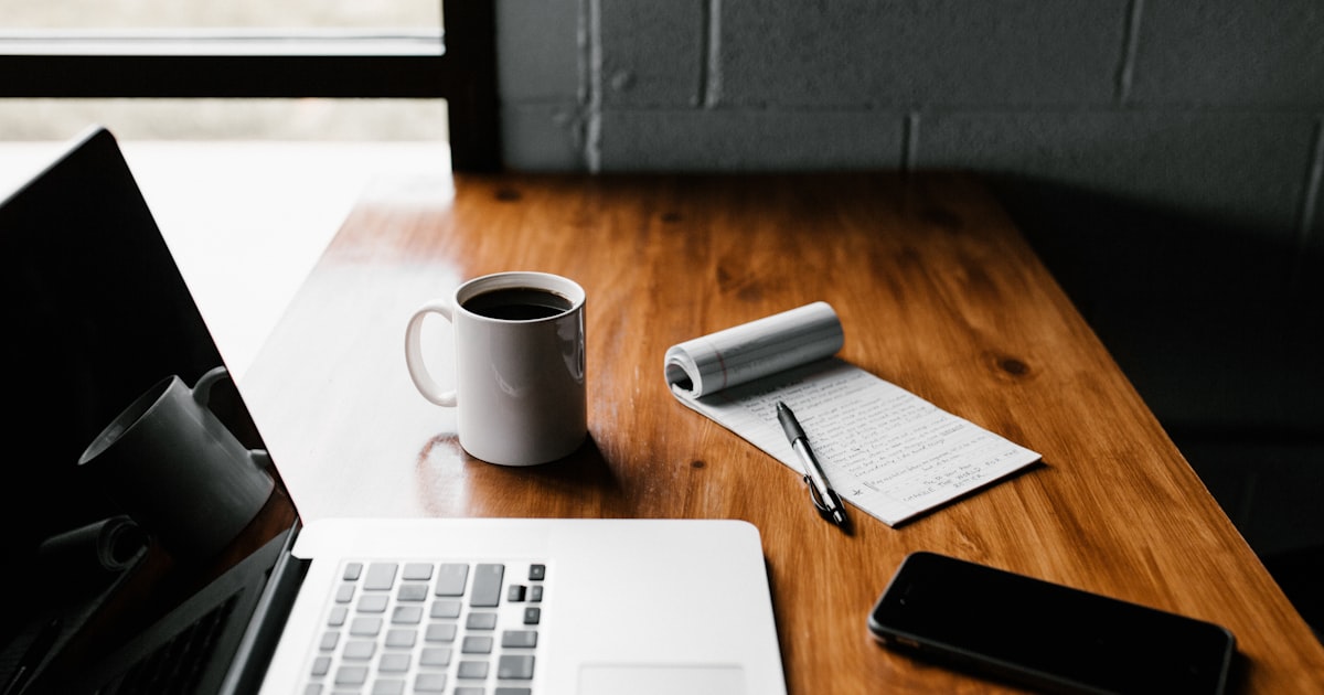 Warm beleuchteter Schreibtisch mit Laptop, Notizbuch und Kaffeetasse – Sinnbild für GEO-/SEO-Arbeit im Mittelstand